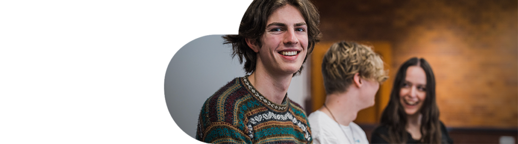 Young male college student smiling and sitting with other students