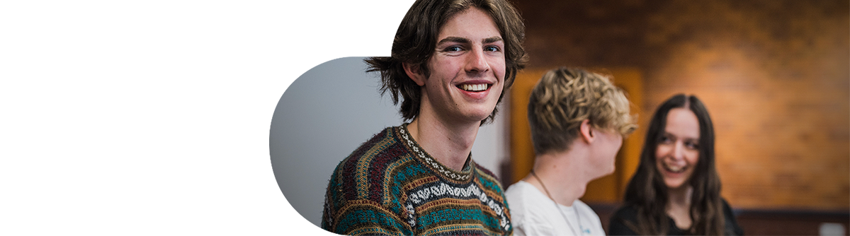 Young male college student smiling and sitting with other students