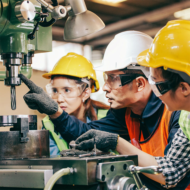 Engineering teacher teaching two students how to use milling machine