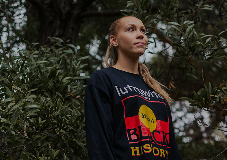 Young Tasmanian Aboriginal woman standing in front of native trees