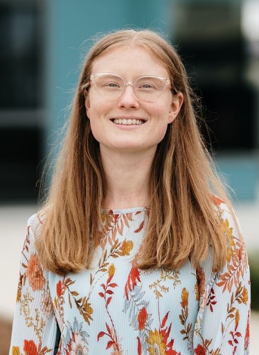 Young woman with long hair and glasses smiling at camera