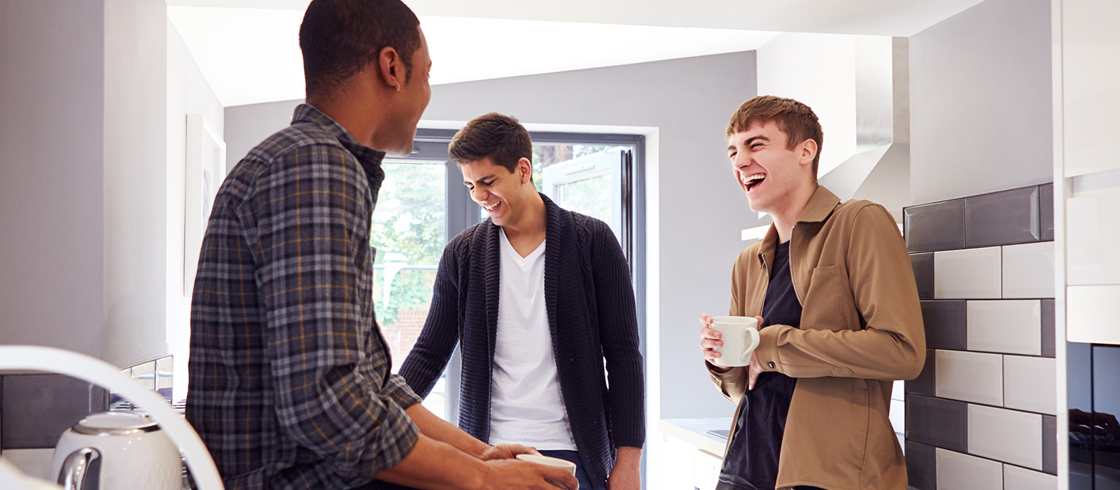 Group Of Male College Students In Shared House With Hot Drinks In Kitchen Hanging Out Together