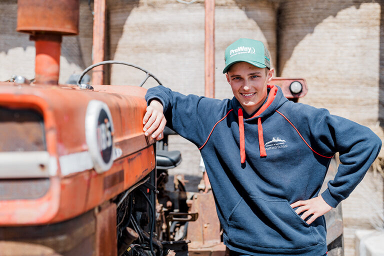 Young male student leaning against a tractor