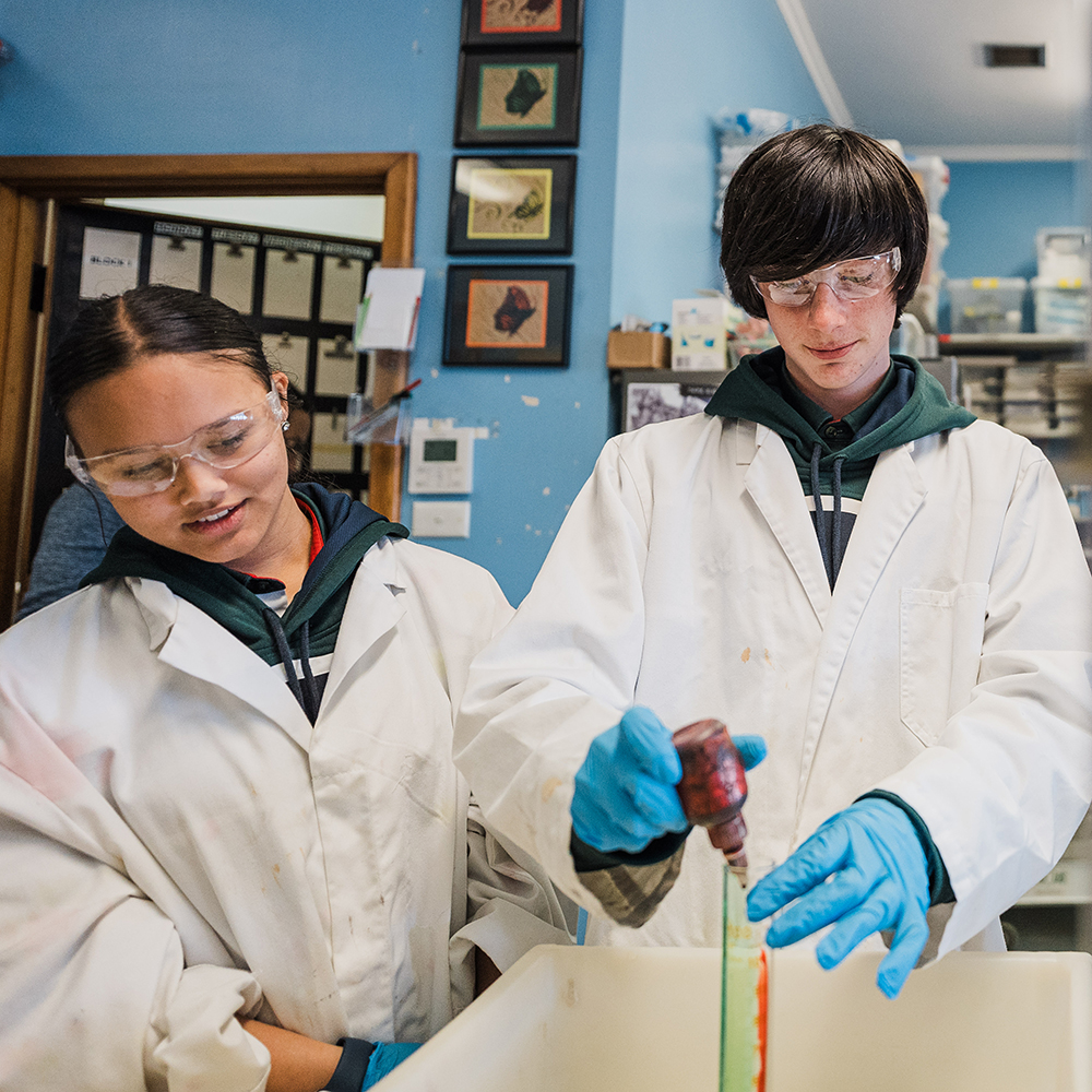 Two teenage students dressed in white lab coats conducting a science experiment