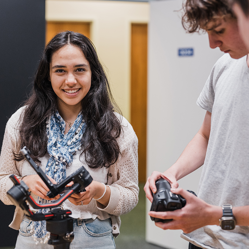Young female student holding camera equipment and smiling at the camera