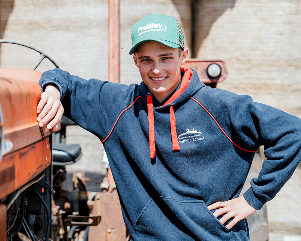 Teenage male student with hat on leaning against a tractor smiling