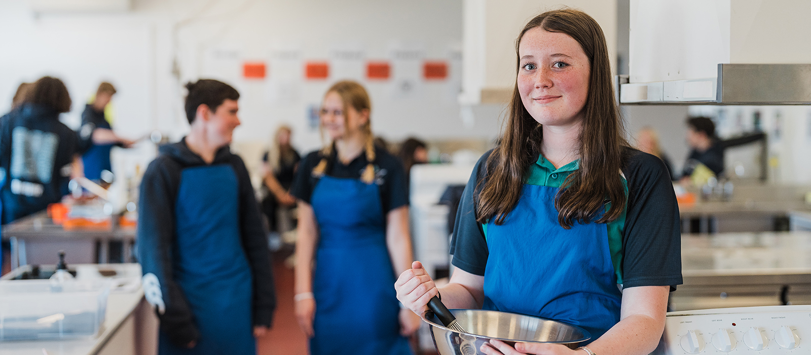 Female teenager holding mixing bowl in commercial kitchen
