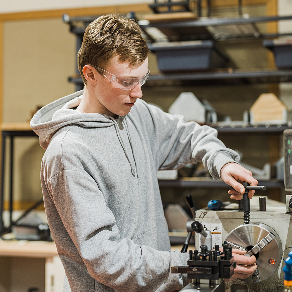 Male teenager using metal lathe in machine shop at school