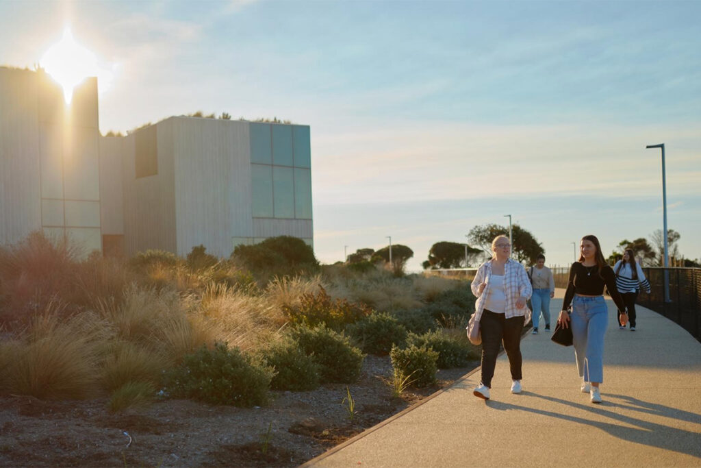 Two students walking along a boardwalk in the sunshine