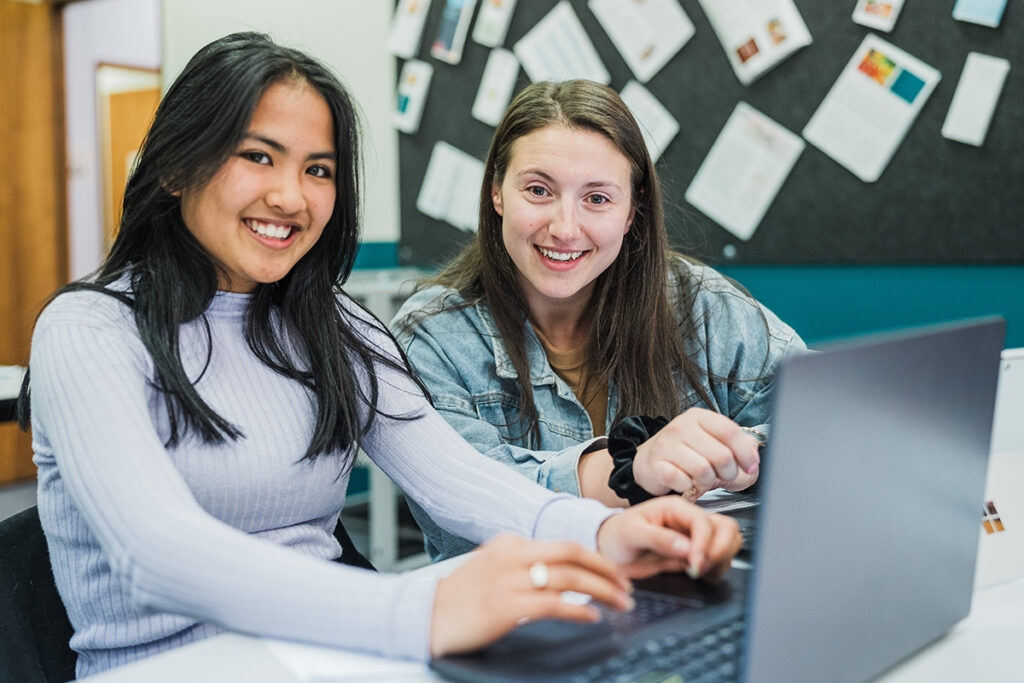 Two female students working at a computer and smiling at the camera