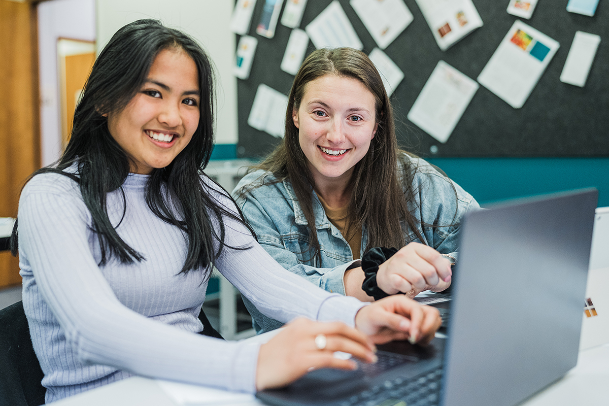 Two female students working at a computer and smiling at the camera