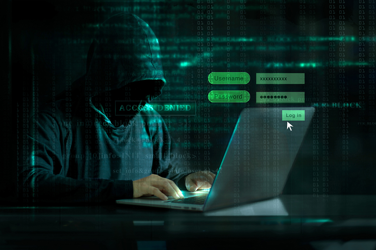 Computer hacker in dark clothing sitting at a computer trying to access systems