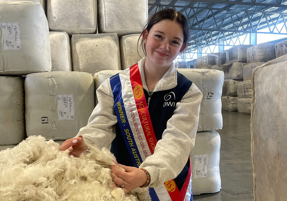 Young female student inspecting wool bales and wearing a champion ribbon