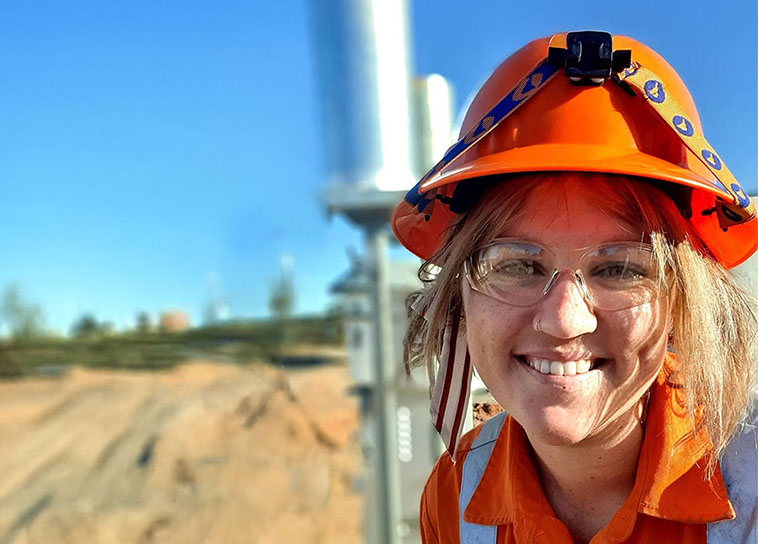 Female miner wearing safety gear smiling at the camera in a sunny outback location