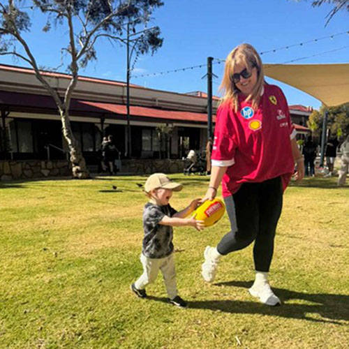Mother walking on grass with small child passing a ball
