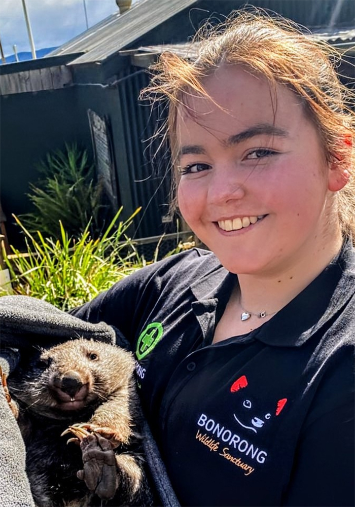 Young female smiling at the camera holding a baby wombat