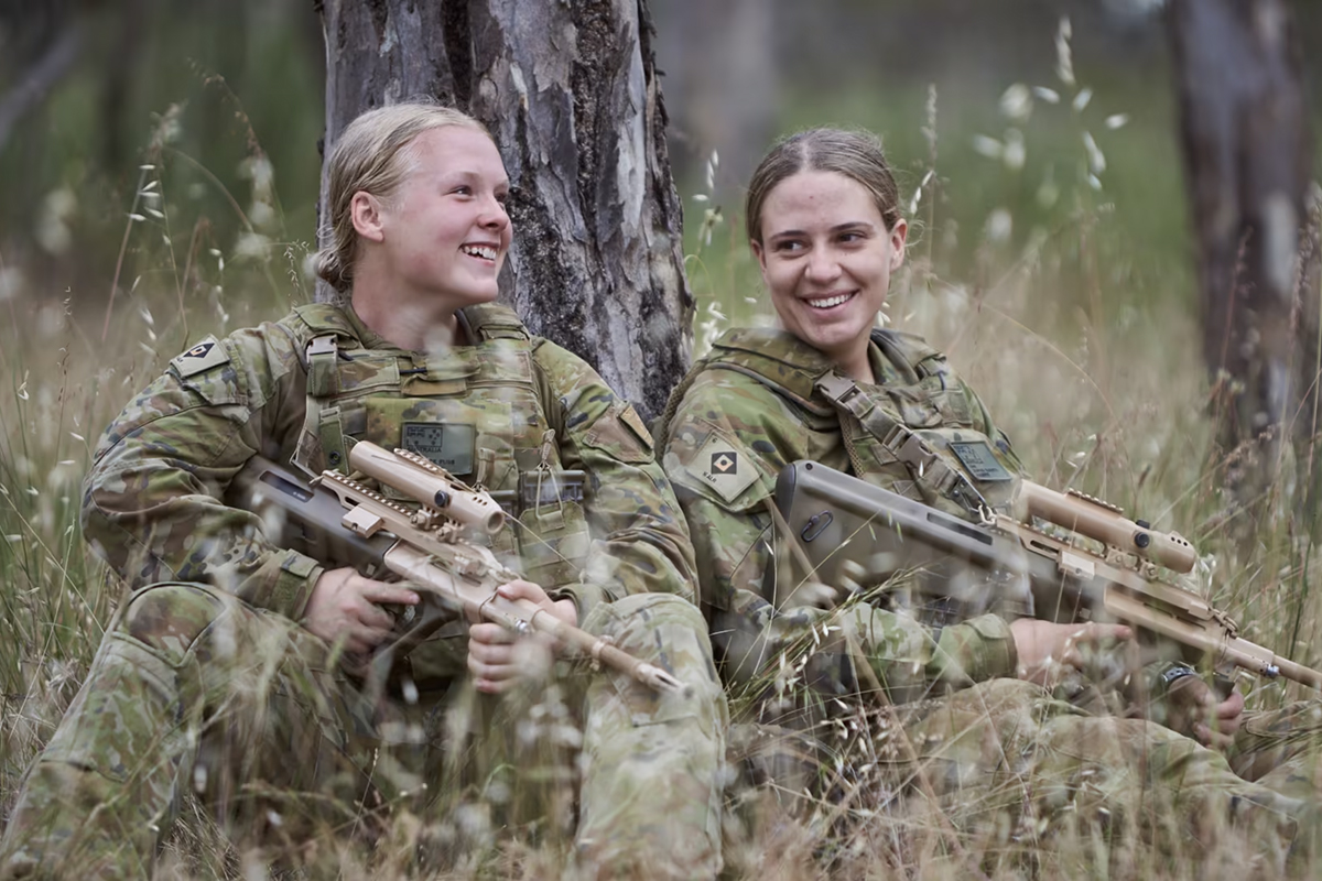 Two young female soldiers sitting against a tree talking