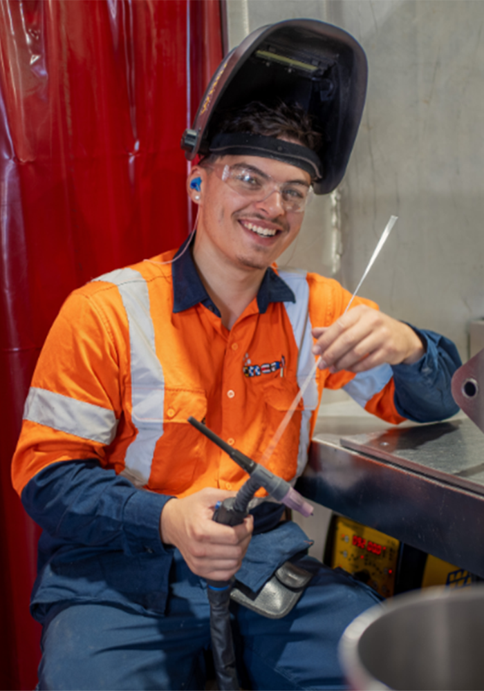 Young male apprentice using a TIG welder and wearing safety equipment