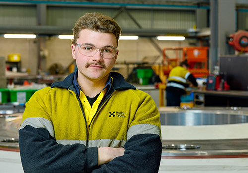 Male tradesperson standing in an industrial workshop with arms folded looking at the camera.